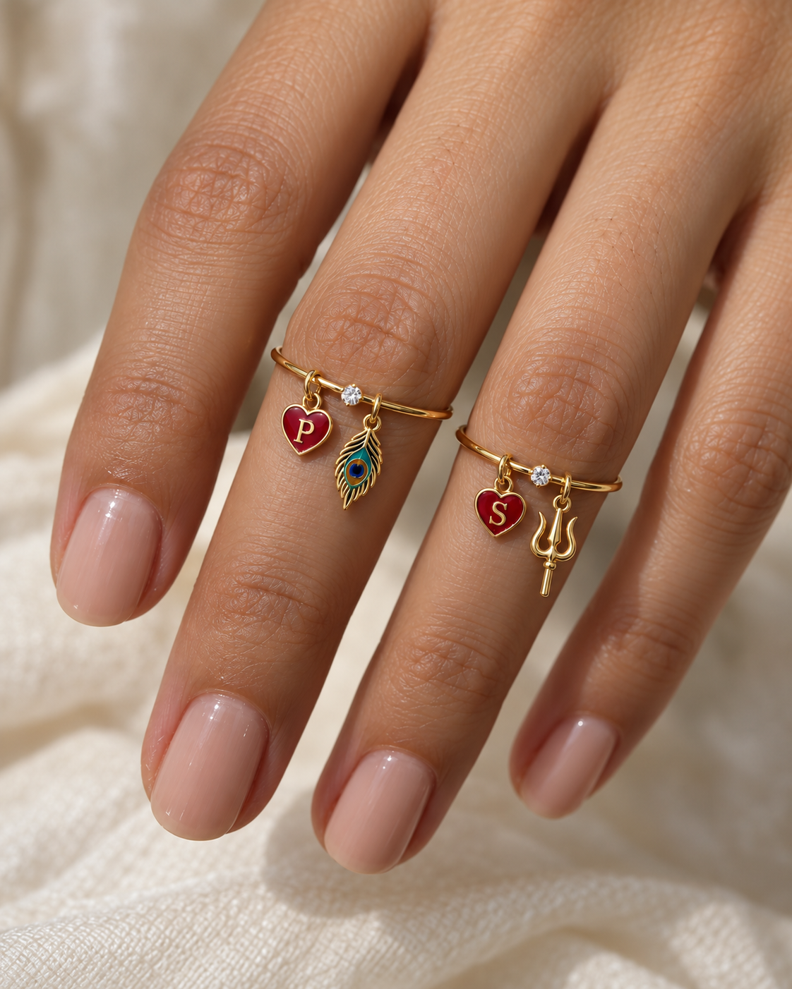 Hari Har Prem Lab Diamond Silver Couple Rings – pair of gold tone charm rings with red enamel heart initials, a gold peacock-feather charm (Krishna) and a gold trishul charm (Shiva), lab grown diamond solitaires, worn on the hand