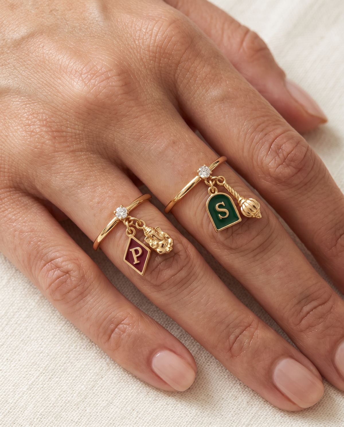 Ekdant Maruti Lab Diamond Silver Couple Rings – pair of gold tone charm rings with maroon enamel diamond-shaped initial and gold Ganesha charm, and emerald-green enamel arch initial and gold gada charm (Hanuman), lab grown diamond solitaires, worn on the hand