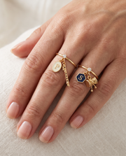 Govind Shankar Lab Diamond Silver Couple Rings – pair of gold tone charm rings with ivory enamel oval initial and gold bansuri charm (Krishna), and navy-blue enamel hexagon initial and gold damru charm (Shiva), lab grown diamond solitaires, worn on the hand