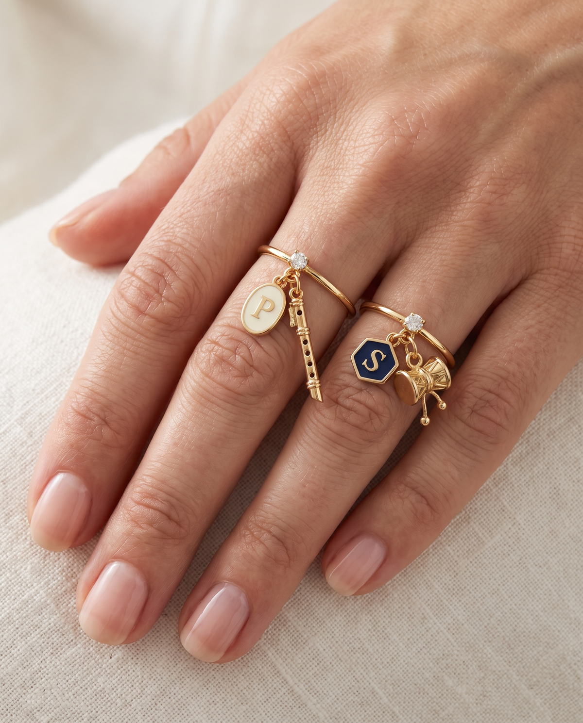 Govind Shankar Lab Diamond Silver Couple Rings – pair of gold tone charm rings with ivory enamel oval initial and gold bansuri charm (Krishna), and navy-blue enamel hexagon initial and gold damru charm (Shiva), lab grown diamond solitaires, worn on the hand