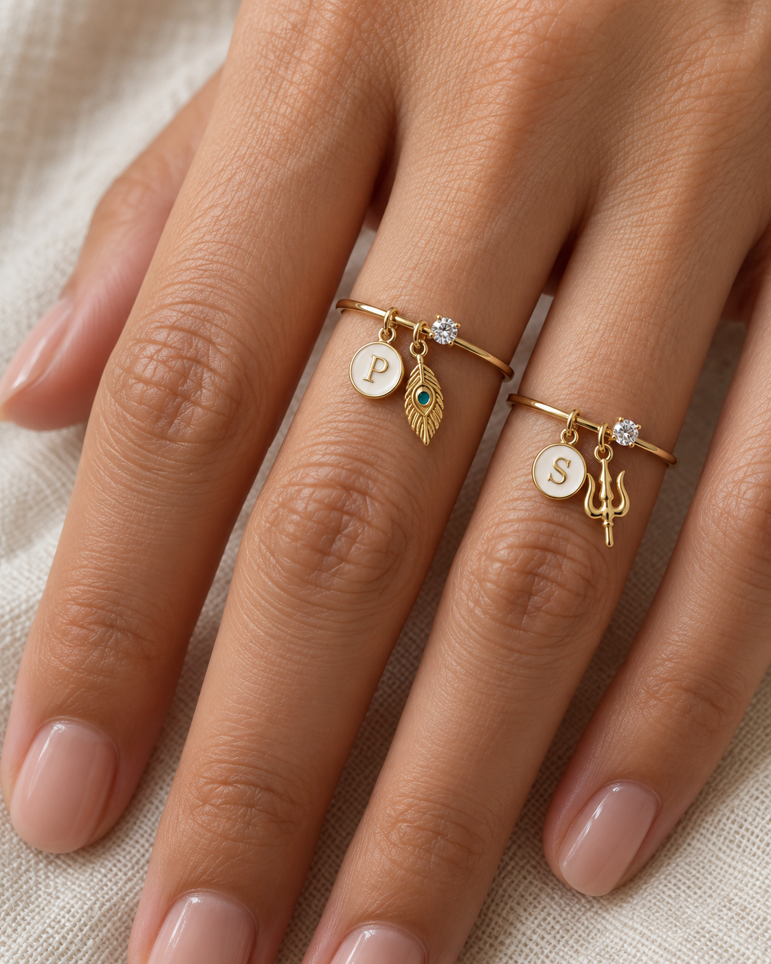 Hari Har Moti Lab Diamond Silver Couple Rings – pair of gold tone charm rings with ivory enamel round disc initials, a gold peacock-feather charm (Krishna) and a gold trishul charm (Shiva), lab grown diamond solitaires, worn on the hand