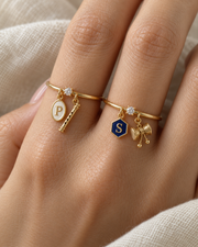 Murli Damru Lab Diamond Silver Couple Rings – pair of gold tone charm rings with ivory enamel oval initial and gold bansuri charm (Krishna), and navy-blue enamel hexagon initial and gold damru charm (Shiva), lab grown diamond solitaires, worn on the hand
