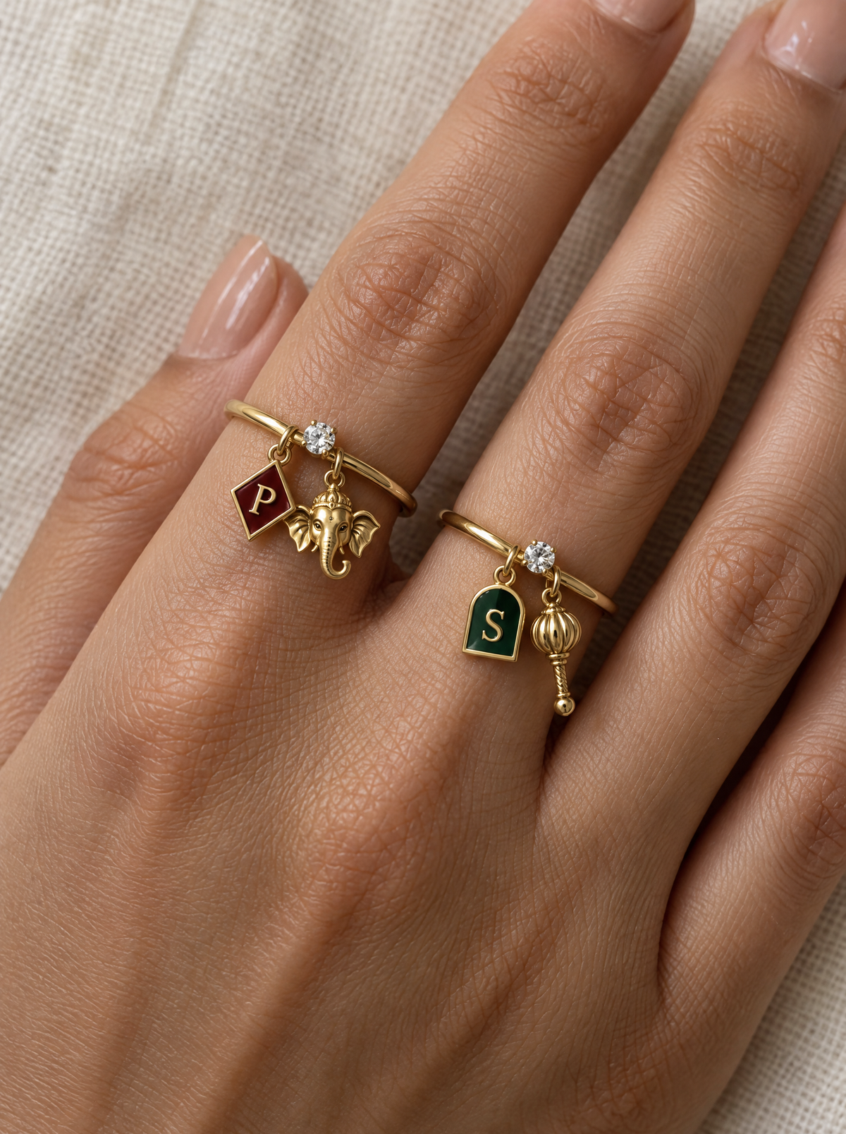 Vighnaharta Sankatmochan Lab Diamond Silver Couple Rings – pair of gold tone charm rings with maroon enamel diamond-shaped initial and gold Ganesha charm, and emerald-green enamel arch initial and gold gada charm (Hanuman), lab grown diamond solitaires, worn on the hand
