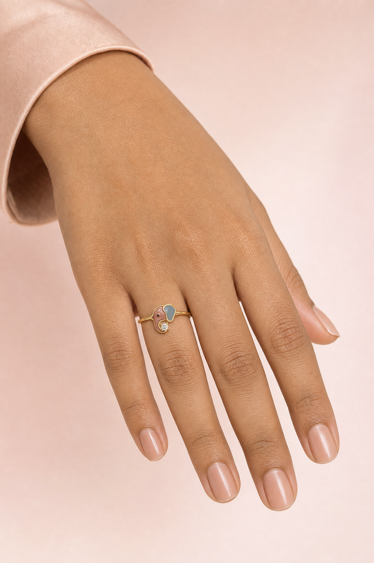 Rosella Twirl ring – rose-pink and sky-blue enamel baby elephant with its trunk curled around a lab grown diamond solitaire, worn on the ring finger