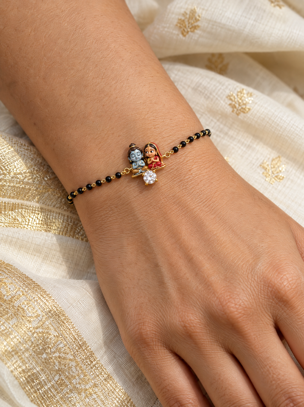 Vandan Shiv Gauri hand mangalsutra – enamel baby Shiva praying with eyes closed and Gauri glancing at him on a gold base with a lab grown diamond, black bead chain on the wrist