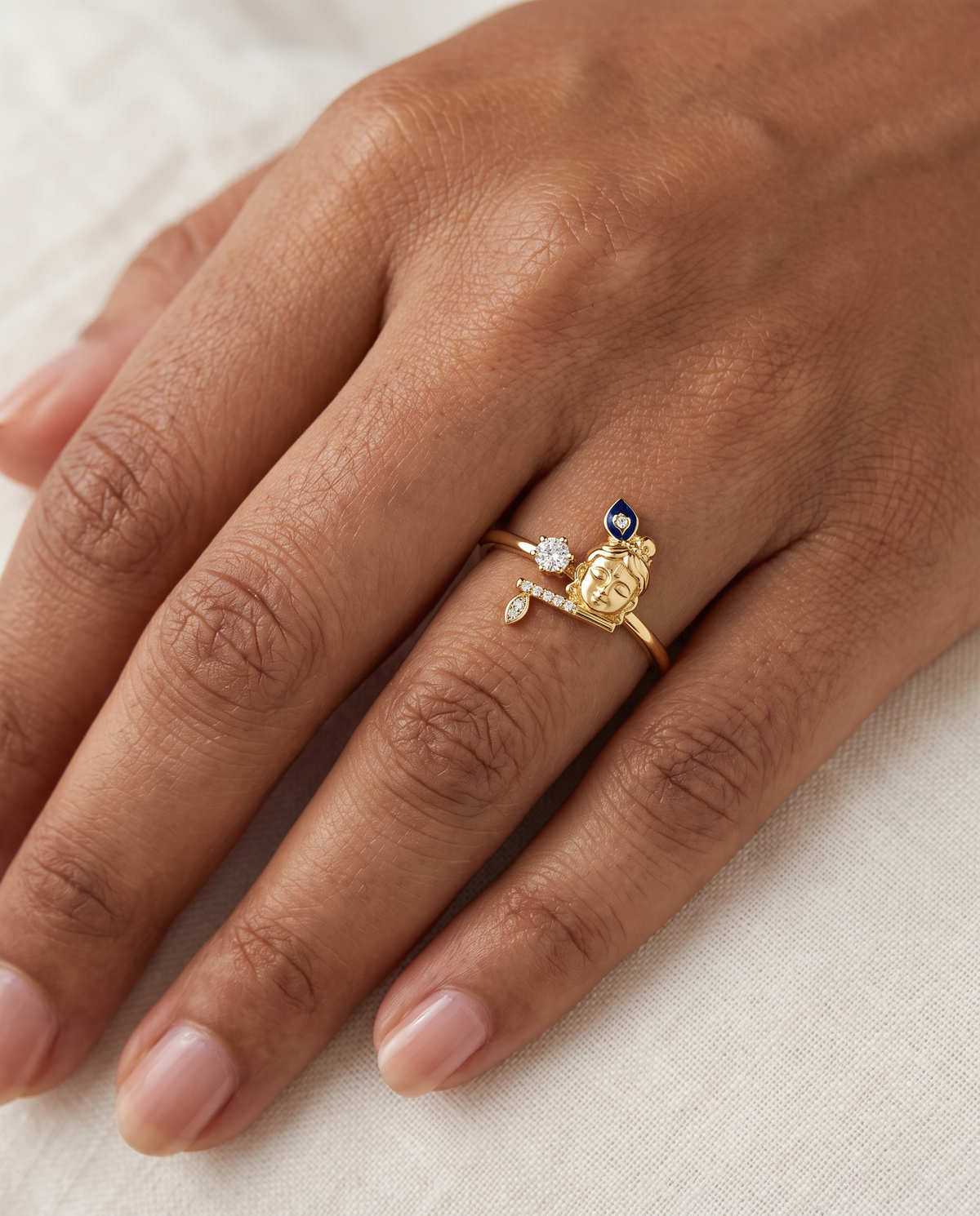 Krishna Gopala ring – Bal Krishna face with a blue enamel peacock feather, diamond-studded flute and leaf, and a lab grown diamond solitaire, worn on the ring finger